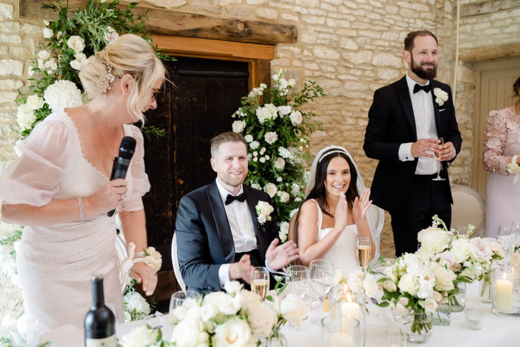a bride and groom are seated and clapping during their wedding speeches at Caswell House