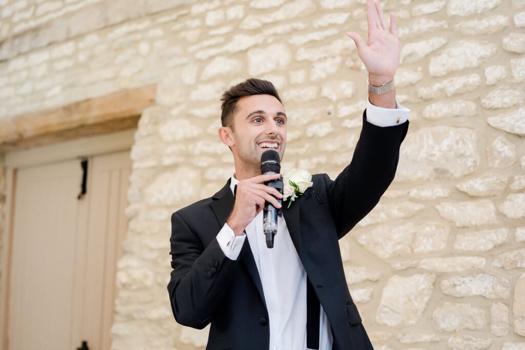 the groom raises his hand during his speech at a wedding at Caswell House