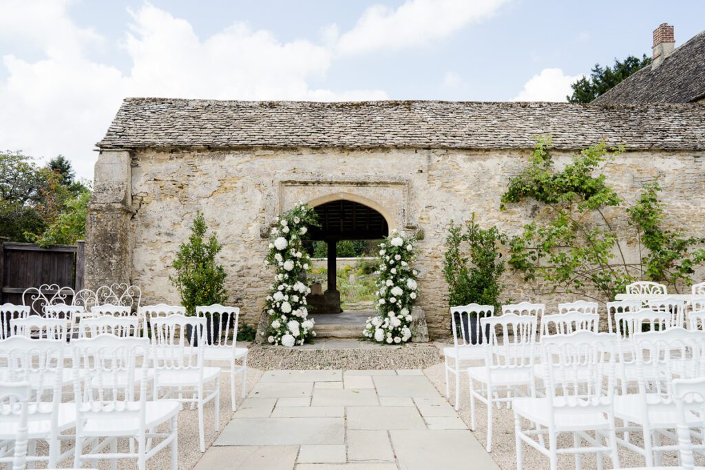 Caswell House set for an outdoor ceremony. White seats lead to a gateway surrounded by flowers.