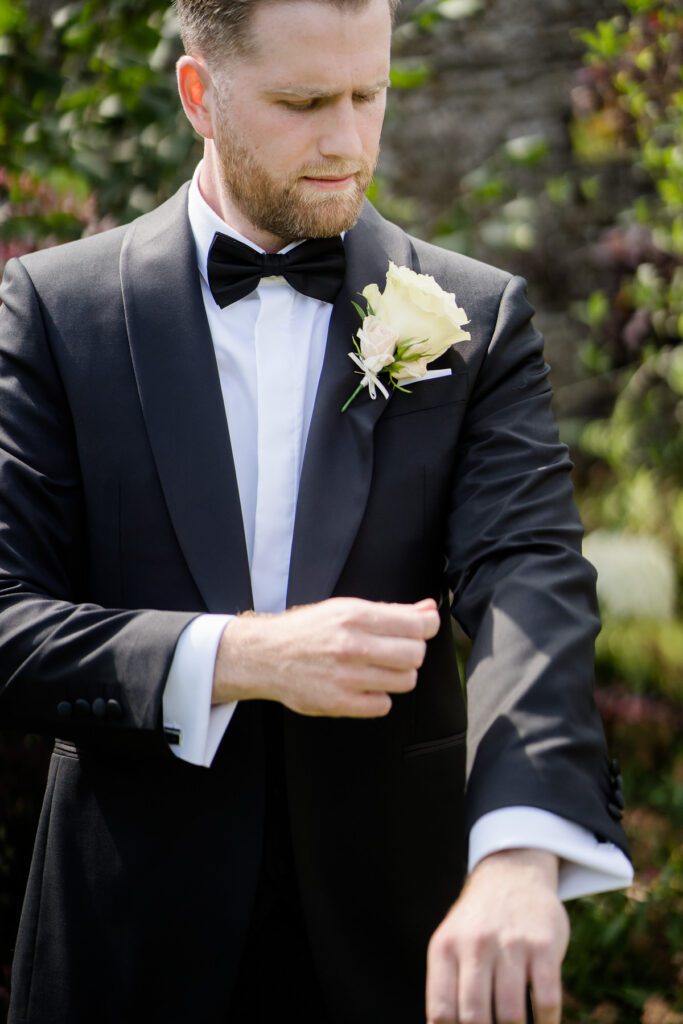 a Groom wearing black tie adjusts his cuffs before his wedding at Caswell House