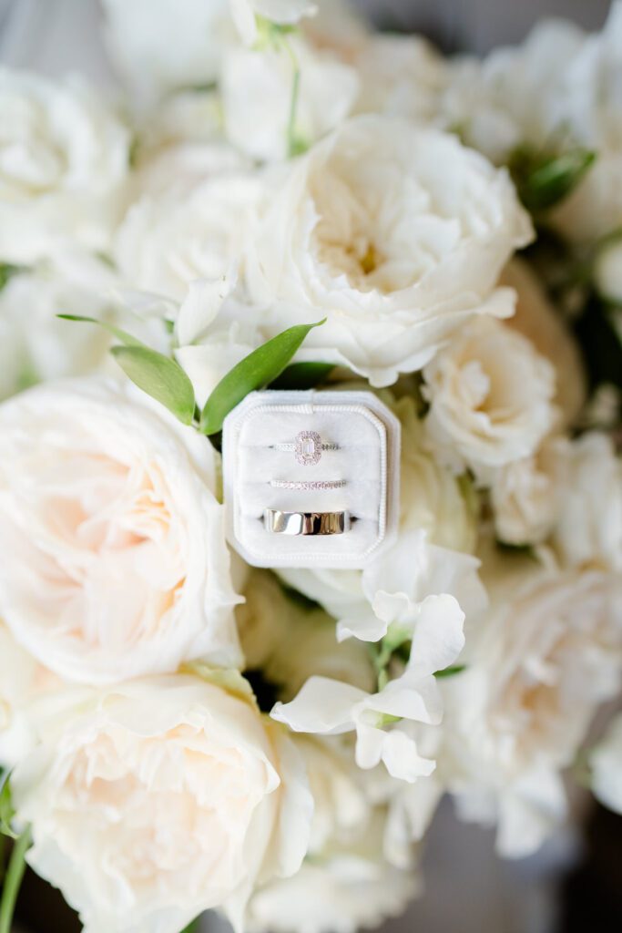 platinum wedding rings in a white velvet box on a backdrop of white roses