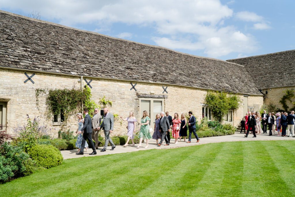 guests walking passed the Cotswold stone barn at Caswell House, the lawn stretches in front of them