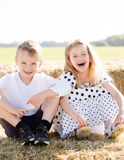 a brother and sister sitting on a hay bail during a family portrait photo shoot in Salisbury