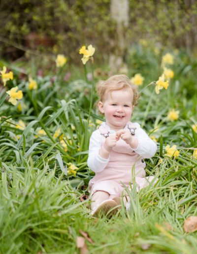 a portrait of a smiling baby girl sitting in daffodils